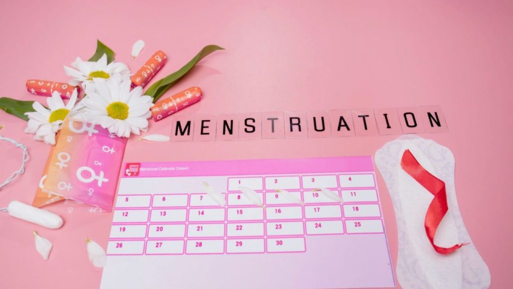 A pink background features a menstruation calendar, highlighting awareness and support for menstrual health and wellness.