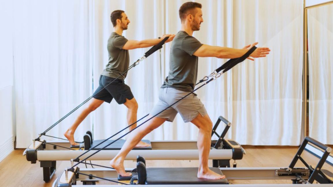 Two men performing Pilates exercises on reformer machines in a fitness studio, promoting physical strength, flexibility, and balance as part of men's wellness routines.