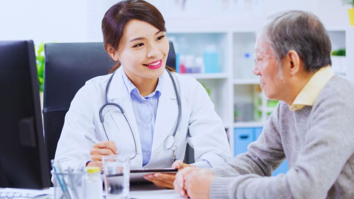 Men’s Wellness: Why Is It Important In A Man’s Life? 1 A female doctor smiling and talking with an older male patient during a consultation, emphasizing the importance of men's wellness and preventive healthcare.