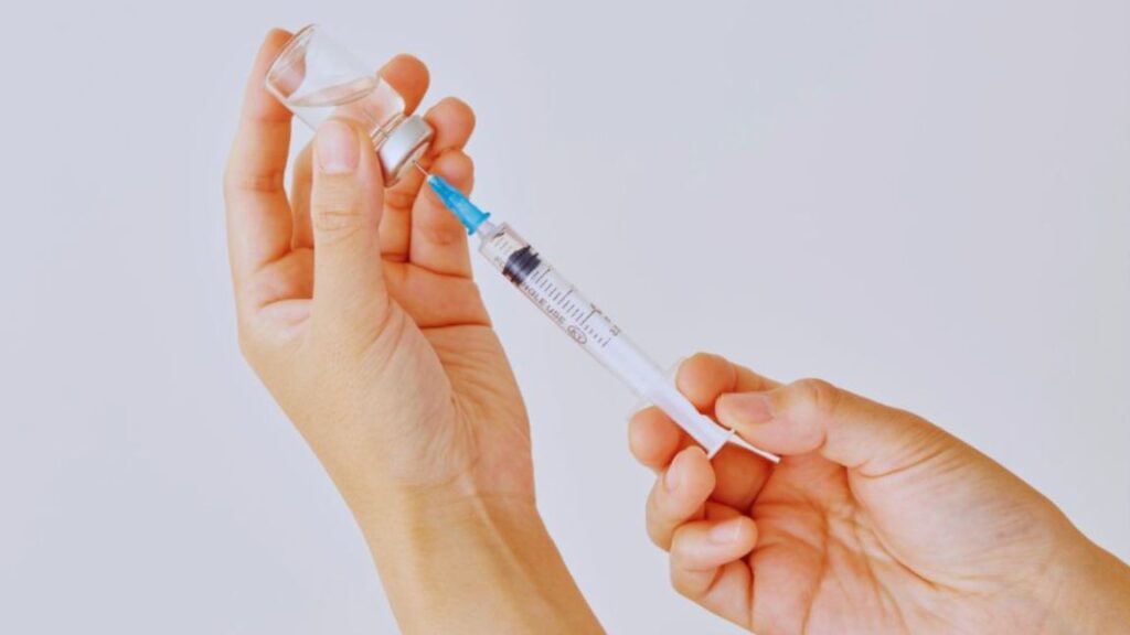 The image shows a person’s hands holding a vial and drawing a clear liquid with a syringe, representing the use of injectable peptides for injury recovery.