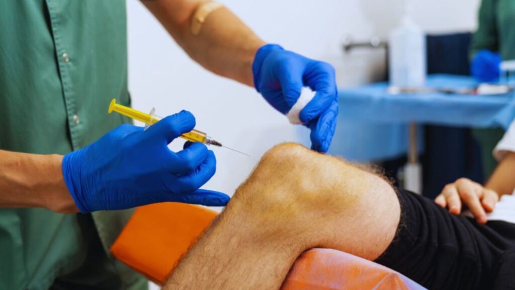 Medical professional administering an injection near a patient’s knee in a clinical setting.