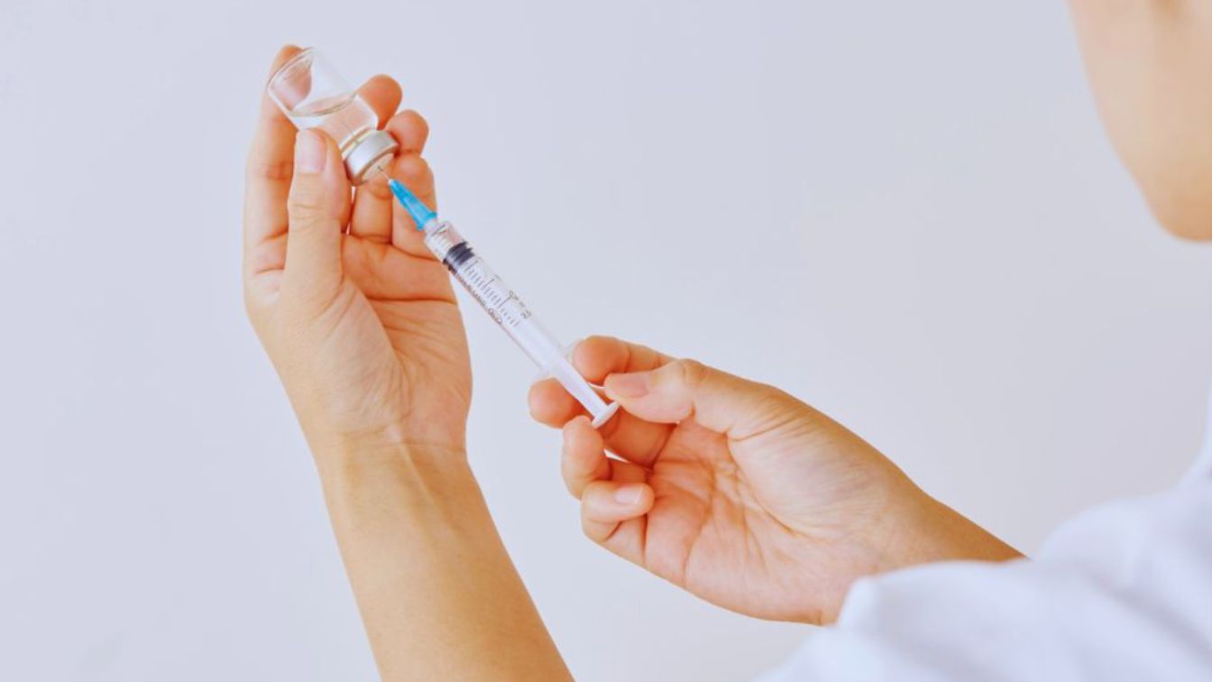 Healthcare professional preparing a syringe and vial in a clinical setting.