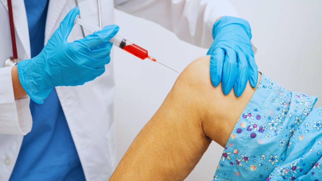 Doctor administering an injection near a patient’s knee during a clinical visit.