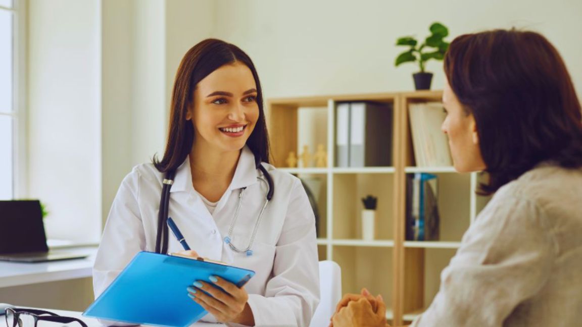 Functional medicine doctor in a white coat holding a clipboard and listening attentively to a patient during a consultation in a bright, modern clinic office.